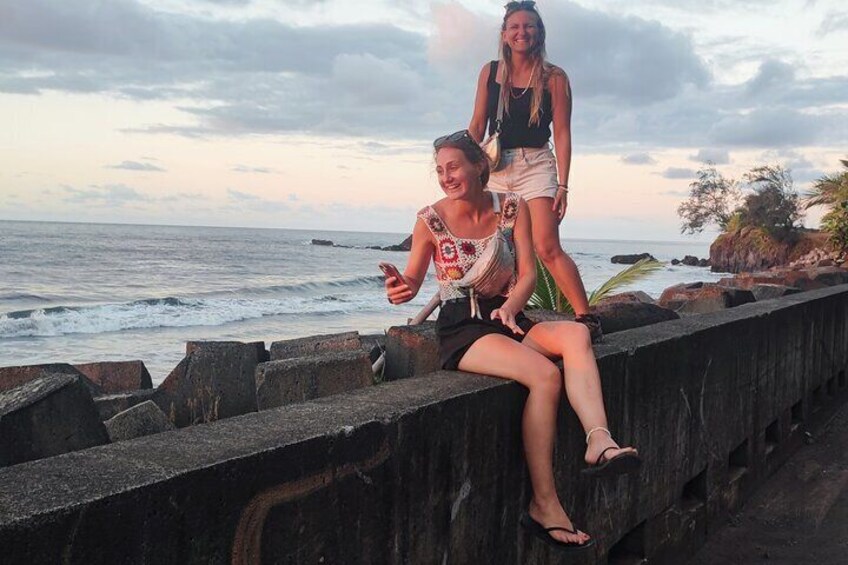 Two people sitting on a concrete barrier by the ocean during sunset. 3