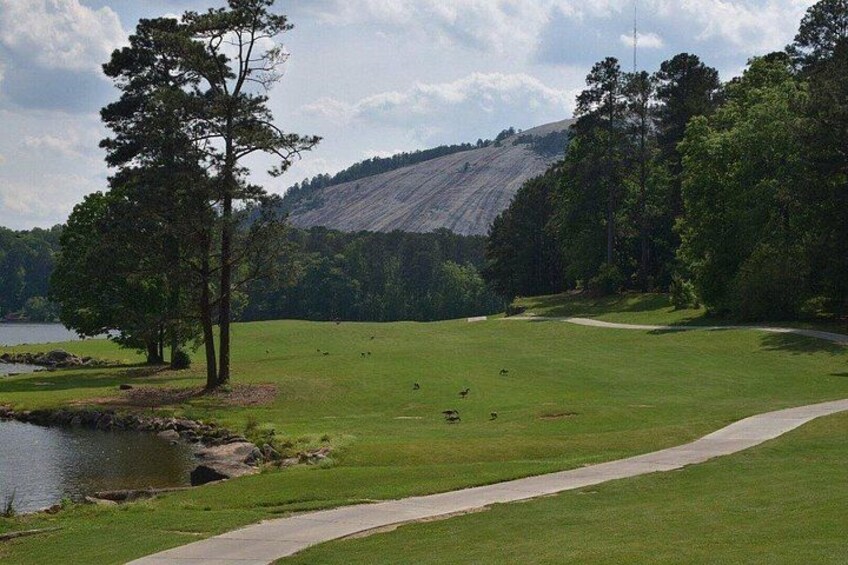 Un campo de golf con un estanque, árboles y un paisaje montañoso al fondo. 2