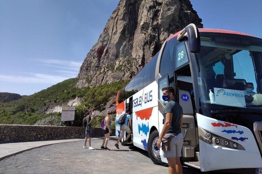 A bus with the number 28 parked near a rocky cliff, people boarding, and a clear sky. 5