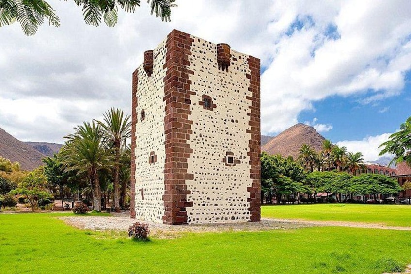 A tower with a brick pattern, surrounded by a green field and palm trees, with mountains in the background. 2