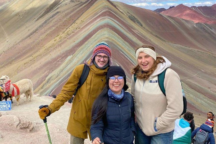 Trois personnes se tiennent debout dans une région montagneuse, devant des formations rocheuses aux couleurs vives. 3