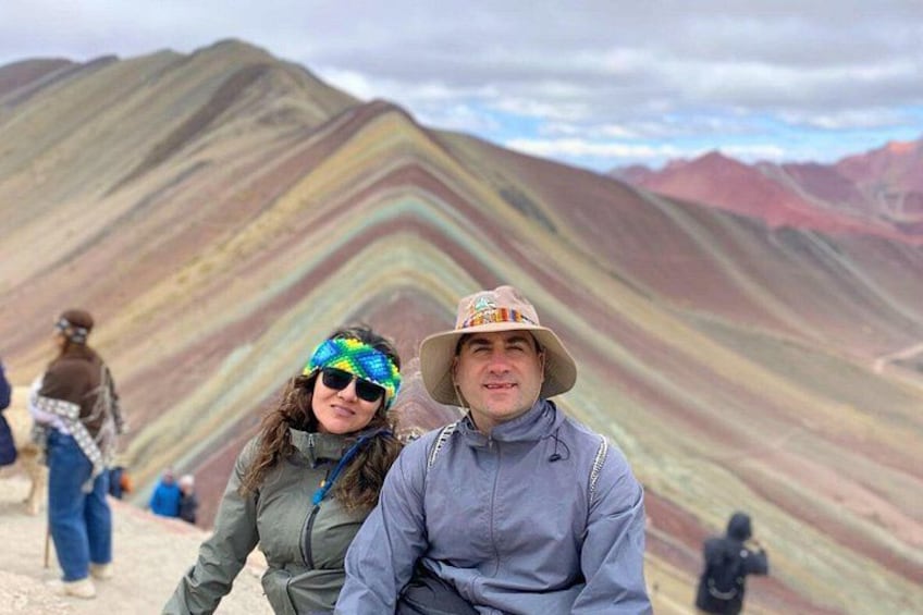 Une personne porte un chapeau et une veste, une autre porte une veste verte, et une troisième porte une veste marron. Les trois sont debout devant une chaîne de montagnes aux couleurs vives. 4