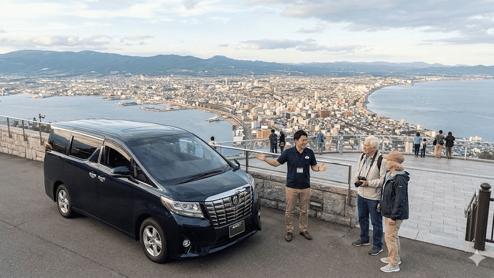 A black van parked by a waterfront with people standing nearby. 1