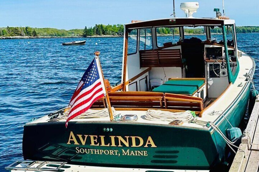 A boat named Avelinda docked at a pier with an American flag, wooden seating, and a view of the water and greenery in the background. 4