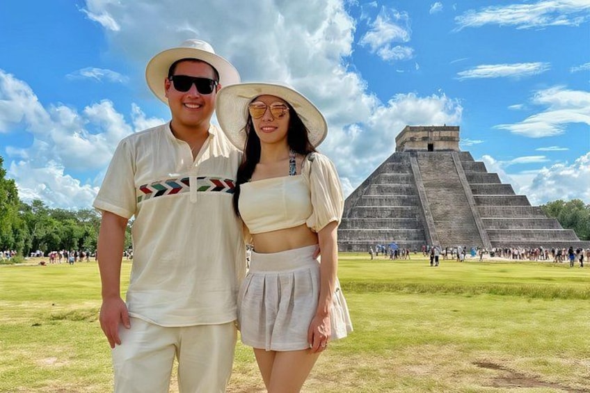 A couple standing in front of a large pyramid with tourists in the background. 1