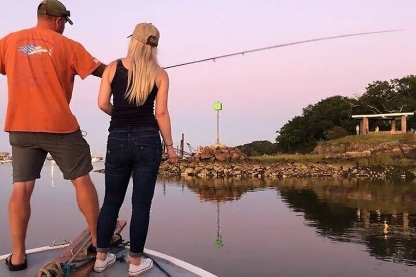 Two people fishing on a boat near a rocky shore with calm water. 4