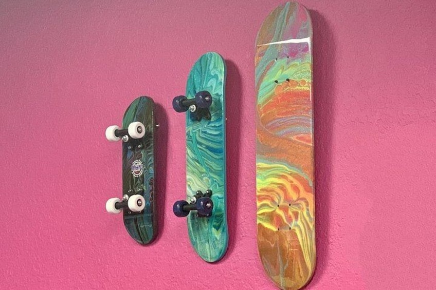 Drie skateboards met kleurrijke designs tegen een roze muur. 2