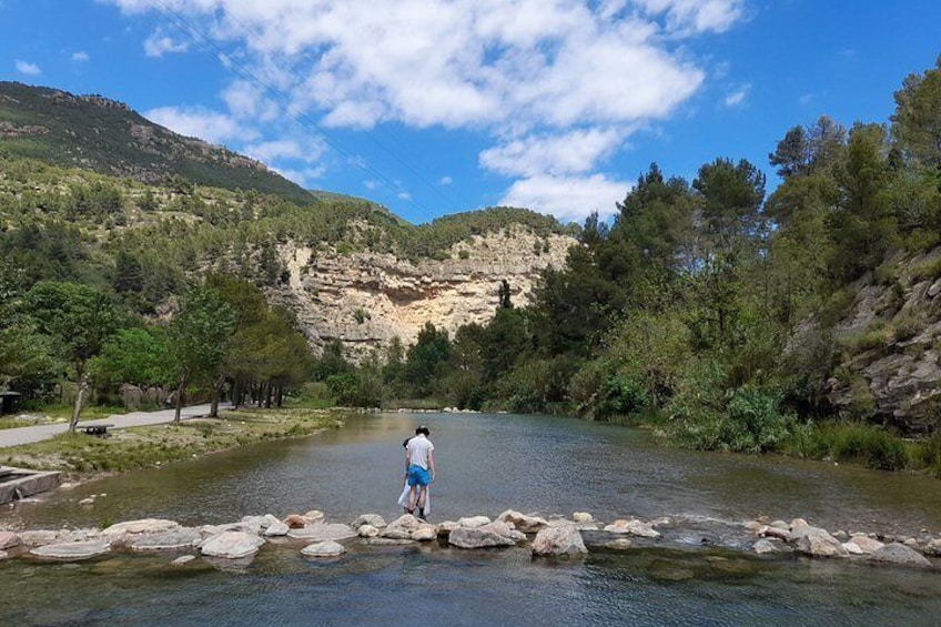 Una persona está de pie sobre rocas junto a un río, con montañas al fondo. 3