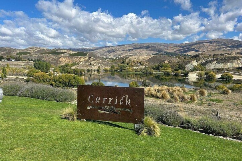 Segnale con la scritta 'Carrick' in una zona erbosa, con un lago e delle colline sullo sfondo. 4
