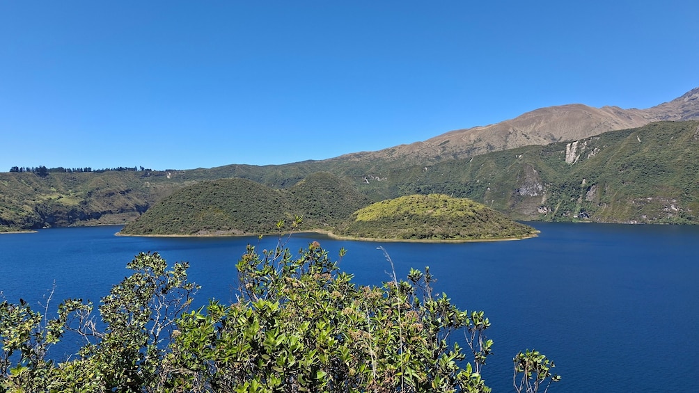 A lake surrounded by green hills and mountains under a clear blue sky. 3