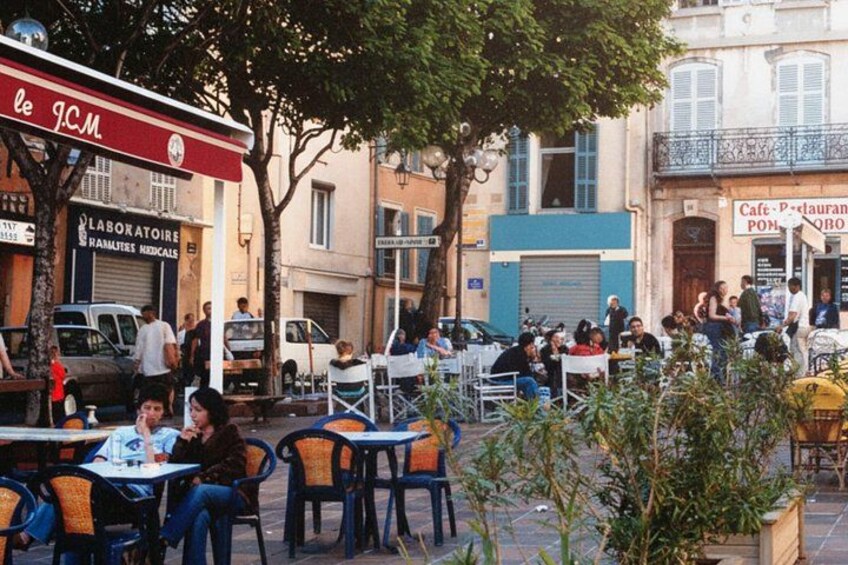 Udesiddeplads ved en café med gæster, et skilt til et medicinsk laboratorium, og en blå bygning med balkon. 2