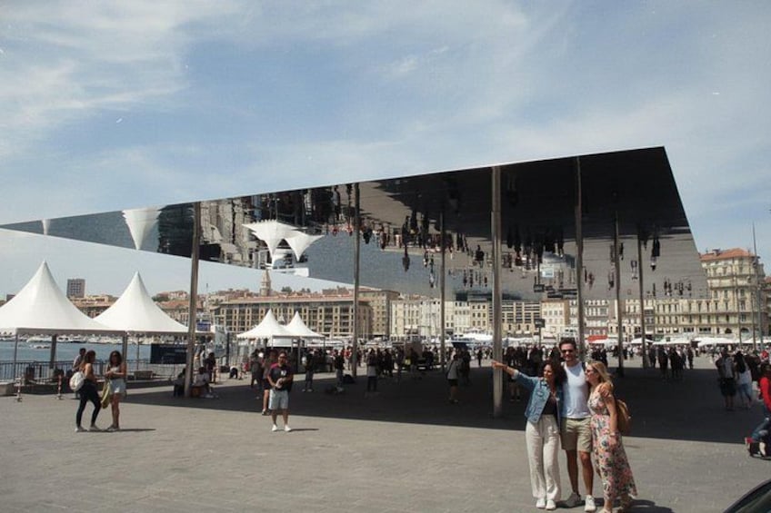 En moderne bygning med et reflekterende facade, havnefront og en menneskemængde. 4