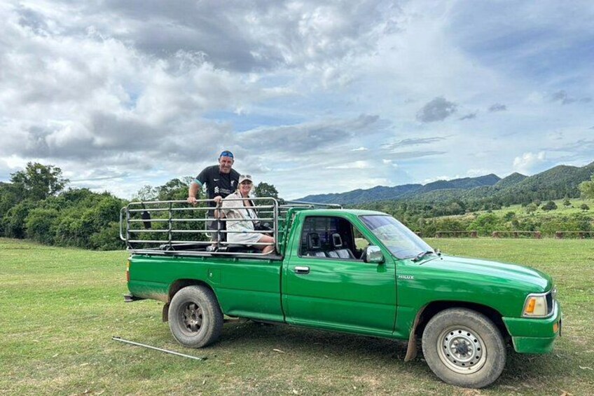 Una camioneta verde estacionada en un campo de hierba con montañas al fondo. 1