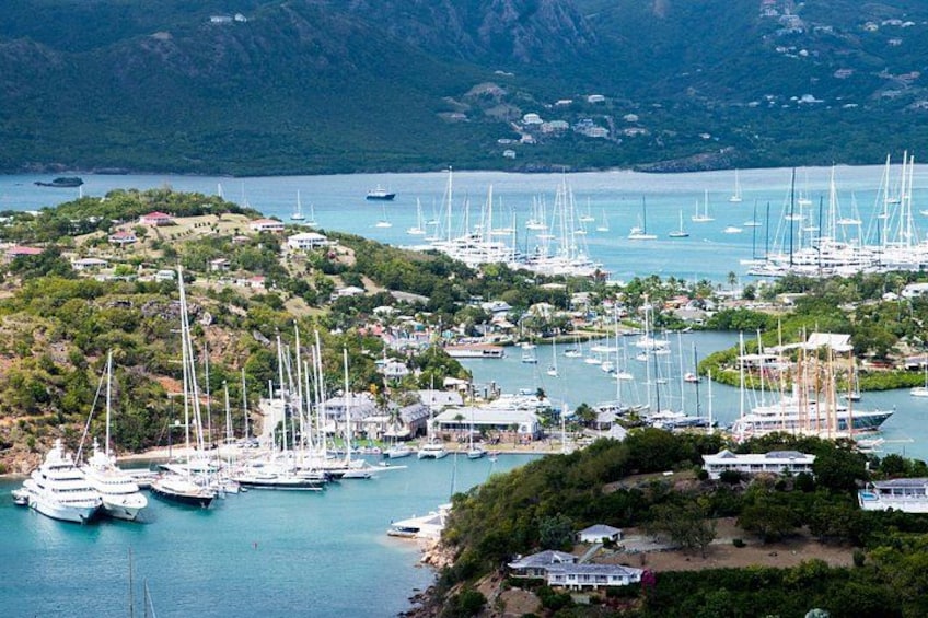 A coastal marina with numerous sailboats docked, surrounded by lush greenery and hills. 2