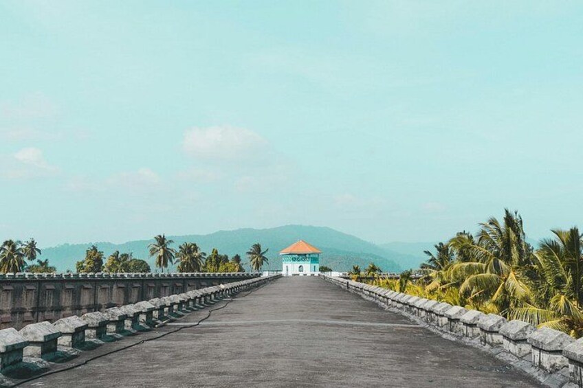 Un puente con un edificio al final, palmeras y montañas al fondo. 3
