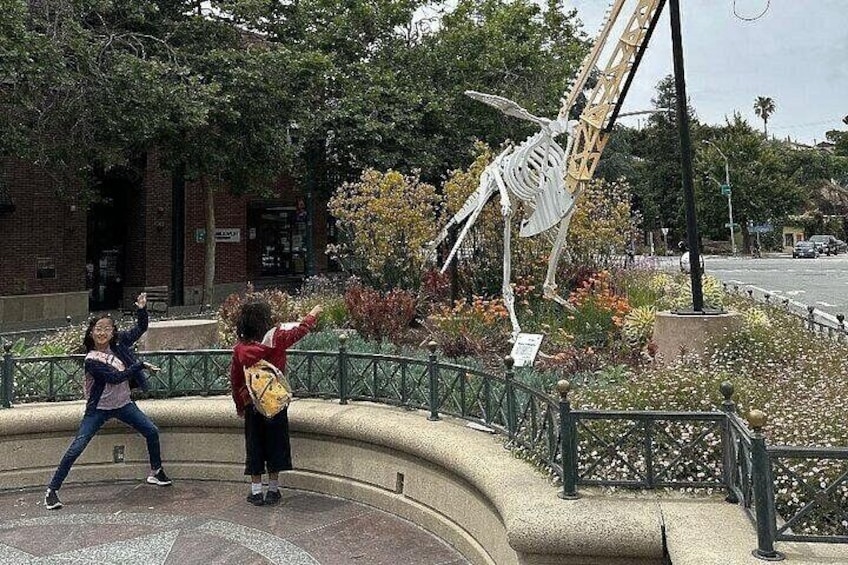 A sculpture of a human skeleton in an outdoor setting with a brick building in the background. 2