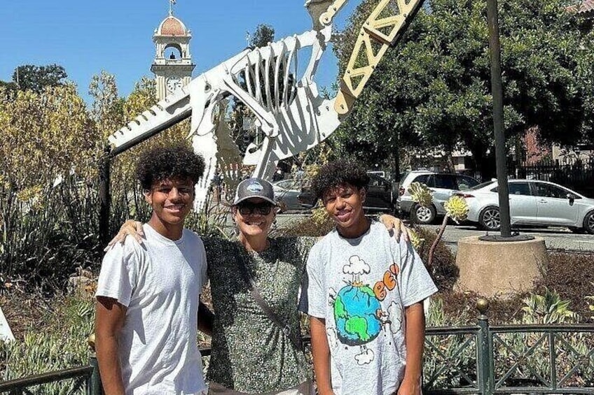 Three people standing in front of a large mechanical structure with a clock tower in the background. 3