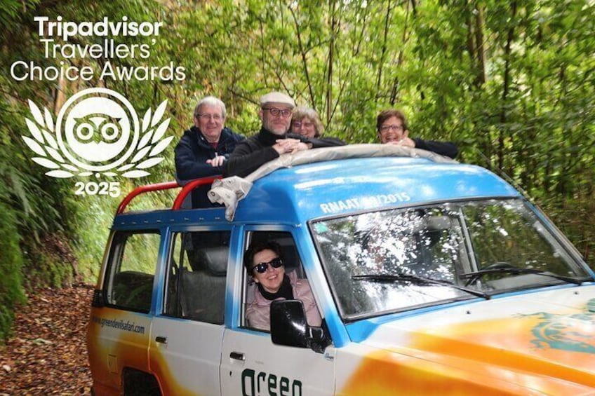 A blue and white vehicle with people on top, surrounded by trees. 2
