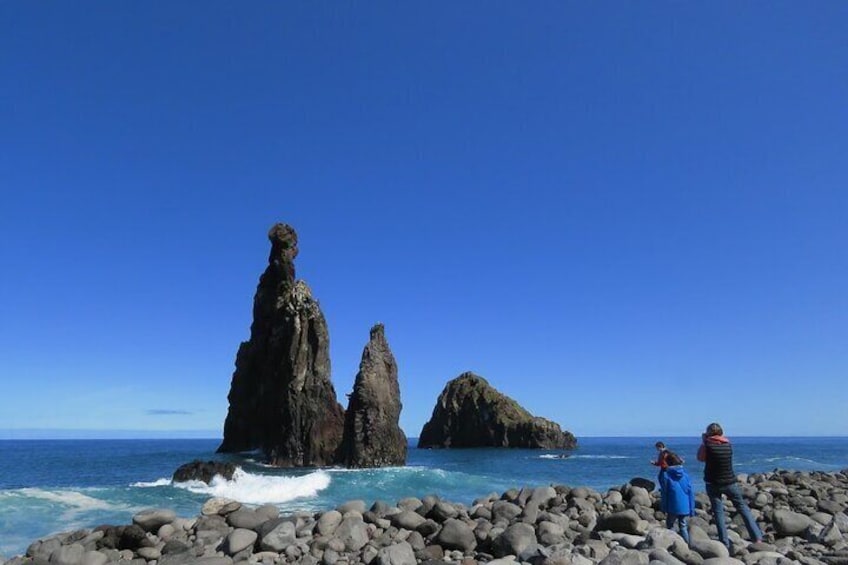 A rocky coastline with two prominent rock formations and a person in a blue jacket standing on the rocks. 4