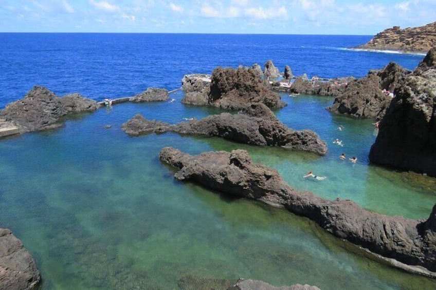 A rocky coastline with clear turquoise water and people swimming. 3