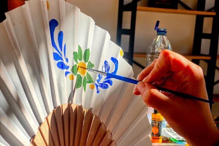 Una mano che dipinge un ventaglio con decorazioni floreali. 1