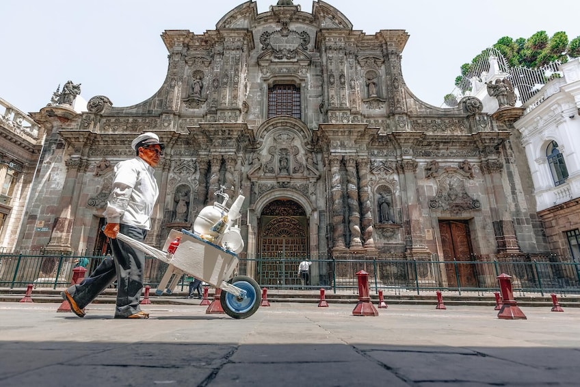 A man pushing a cart with a large container in front of a historic building with ornate architecture. 3