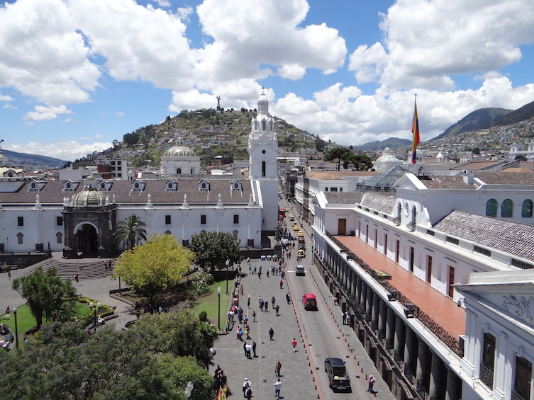 A bustling plaza with a prominent white church, a red car, and a flag. 1