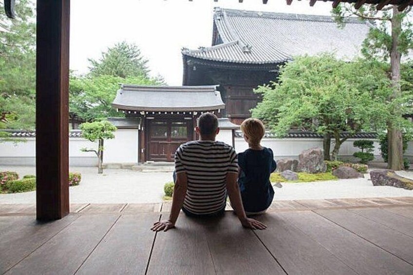 Two people sitting on a wooden floor, facing a traditional Japanese building. 5