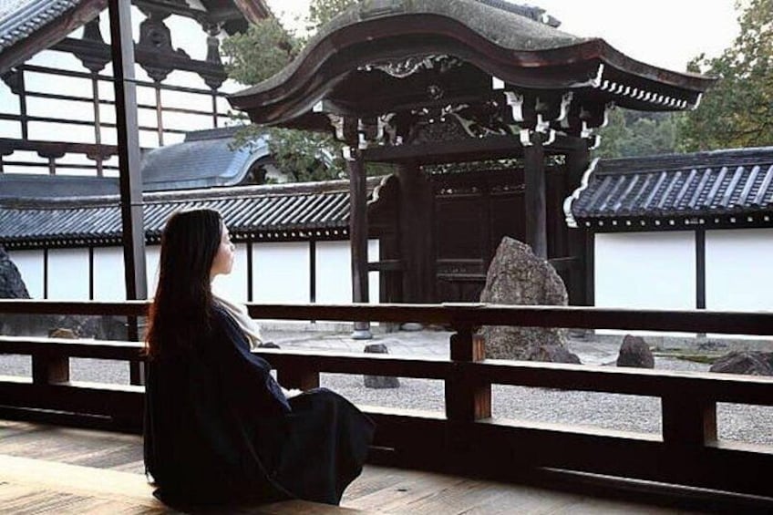 A person sitting on a wooden platform in a traditional Japanese garden with a stone lantern and a wooden pavilion in the background. 4