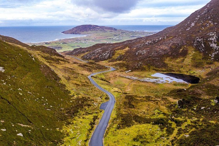 A winding mountain road, a valley, and a distant coastline. 3