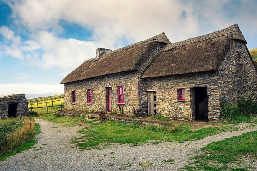 A stone house with a thatched roof, a gravel path, and a yellow fence in the background. 2