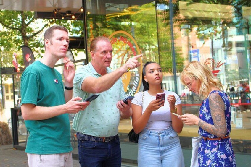 Un groupe de personnes se tient devant un bâtiment à la façade en verre, engagées dans une conversation et utilisant des téléphones portables. 1