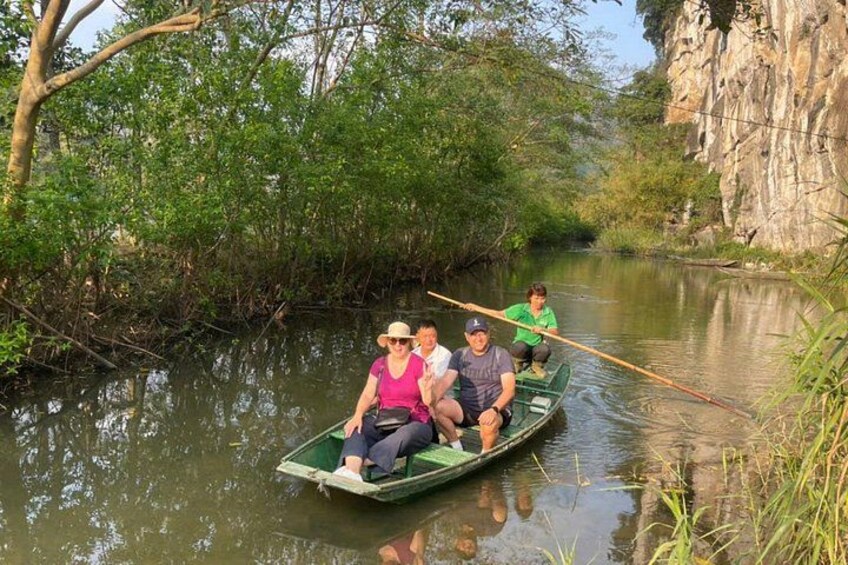 A group of people in a green boat on a calm river surrounded by dense vegetation and cliffs. 2