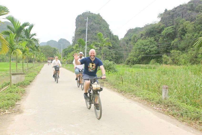 A group of people riding bicycles on a rural road surrounded by greenery and palm trees. 1