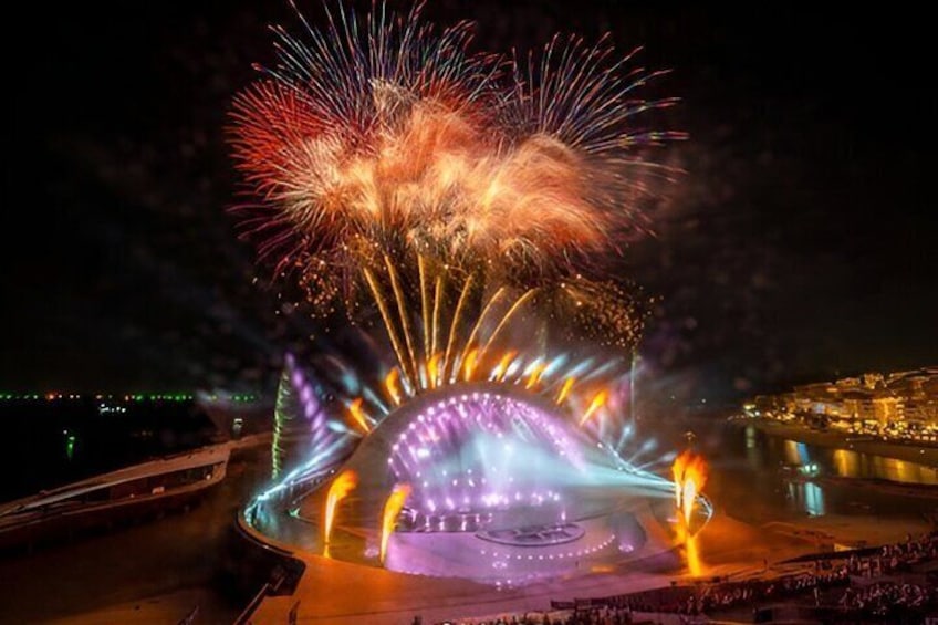 A fireworks display over a circular stage with a crowd in the foreground. 5