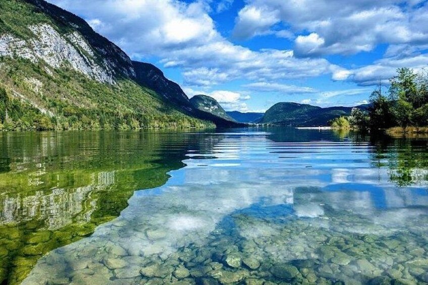 Un lac aux eaux limpides où l’on peut apercevoir des rochers, entouré de montagnes et surplombé d’un ciel partiellement nuageux. 2