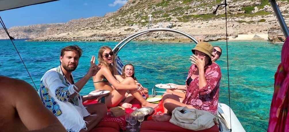 A group of people on a boat in clear blue waters, with rocky cliffs in the background. 1