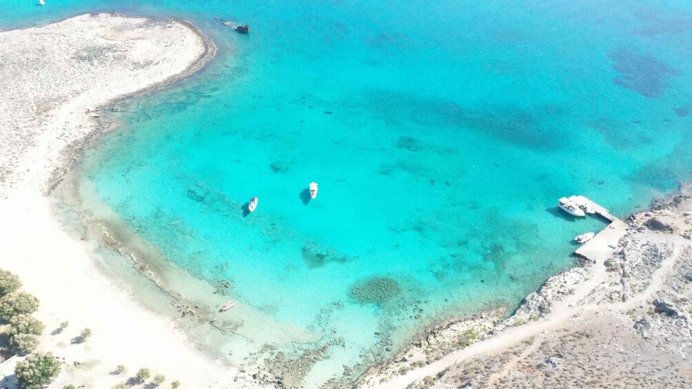 A turquoise sea with boats, a sandy beach, and rocky terrain. 3