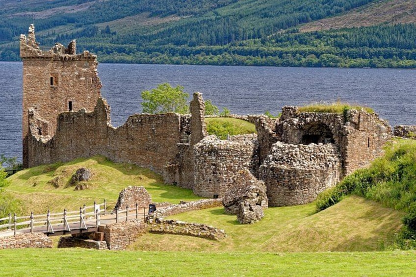 A historic stone castle ruin by a lake with a wooden bridge. 3