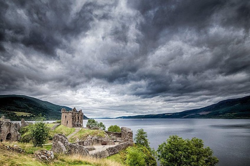 A historic castle ruin by a lake with overcast skies. 1