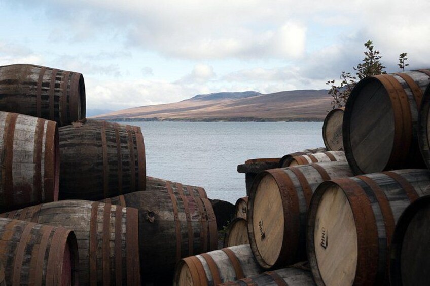 Barrels stacked near a body of water with hills in the background. 4