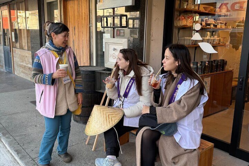 Trois personnes sont assises devant un magasin, et l’une d’entre elles tient une boisson à la main. 1