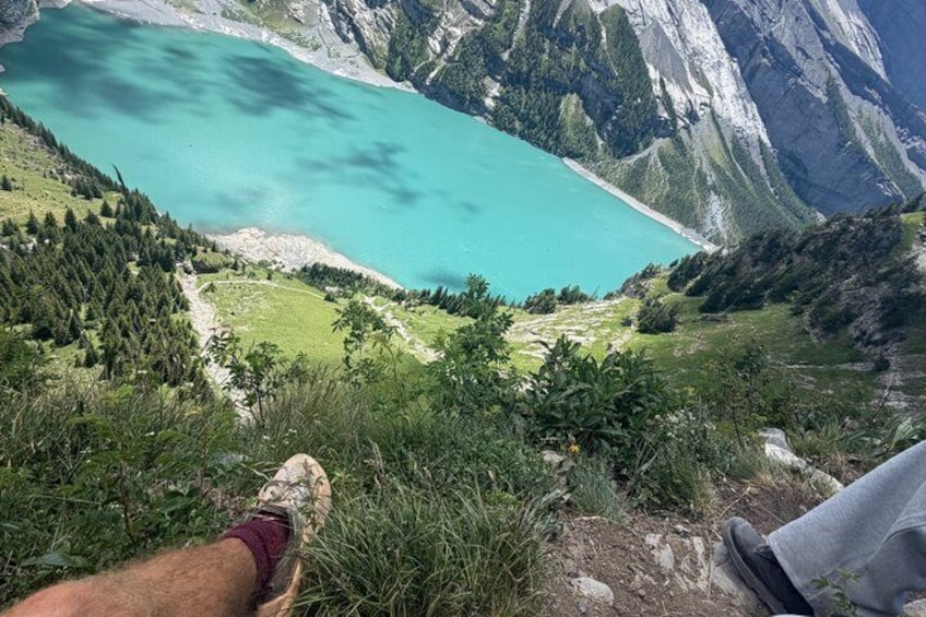 Pies sobre un sendero de montaña con vista a un lago turquesa rodeado de montañas boscosas. 5
