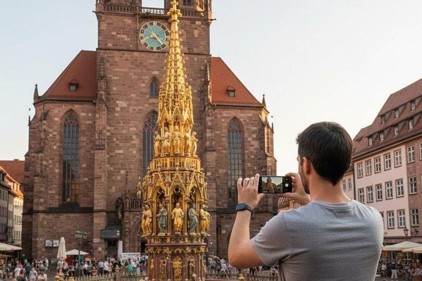 A person taking a photo of a historic church with a tall spire and a golden statue in front. 4