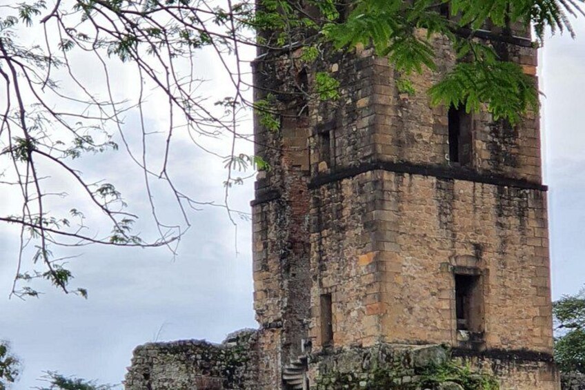 Ein verwitterter Steinturm mit deutlichen Schäden und überwucherter Vegetation. 1
