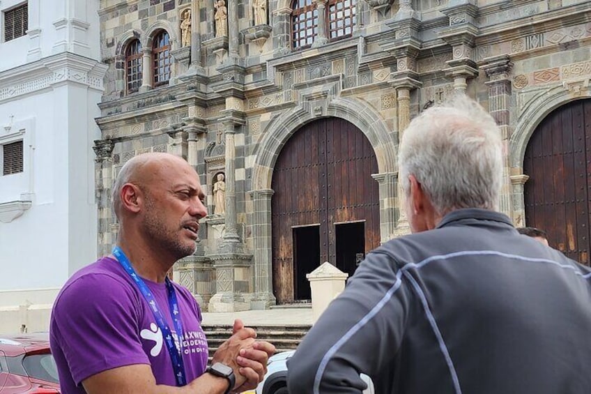 Two men conversing in front of a historic building with ornate architecture and large wooden doors. 2