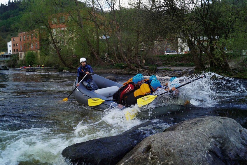 A group of people kayaking on a river with rocks and buildings in the background. 3