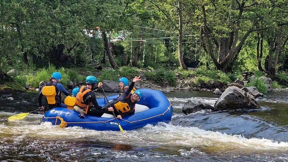 A group of people rafting on a blue inflatable raft in a river surrounded by trees. 4