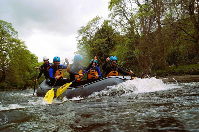 A group of people in a raft navigating a river surrounded by trees. 2