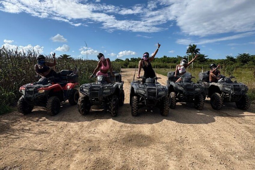 Four people on ATVs on a dirt path with vegetation on the sides. 1